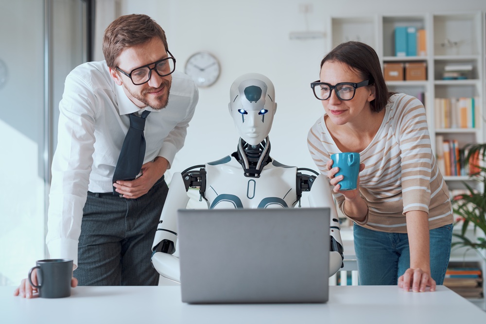 man and woman standing over a robot which is working on a laptop