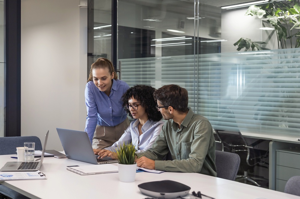 a man and 2 women sitting at a desk working on a laptop