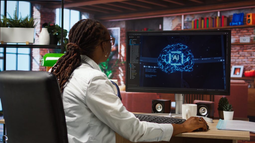 Professional with dreadlocks reviewing glowing digital brain AI graphics and software code on desktop monitor.